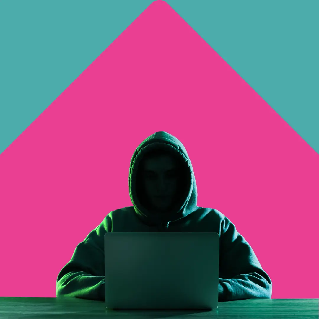 Person in a hooded sweatshirt working on a laptop with a teal and pink background.