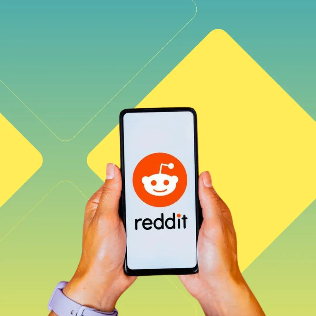 A hand holding a mobile phone with the Reddit logo on the screen.